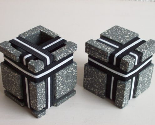 Two square stoneware cubes with nine elastics each.